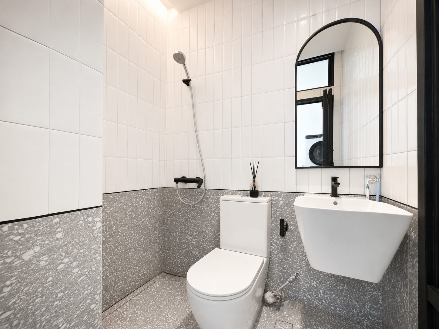 The second bathroom, white tile with a terrazzo floor and an arched black mirror