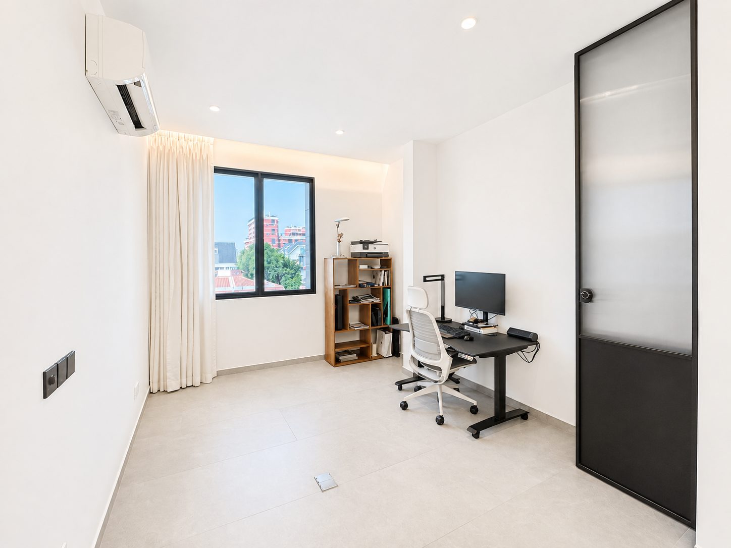 The second bedroom, currently set up as a study, with a black-framed frosted glass sliding door to the living room